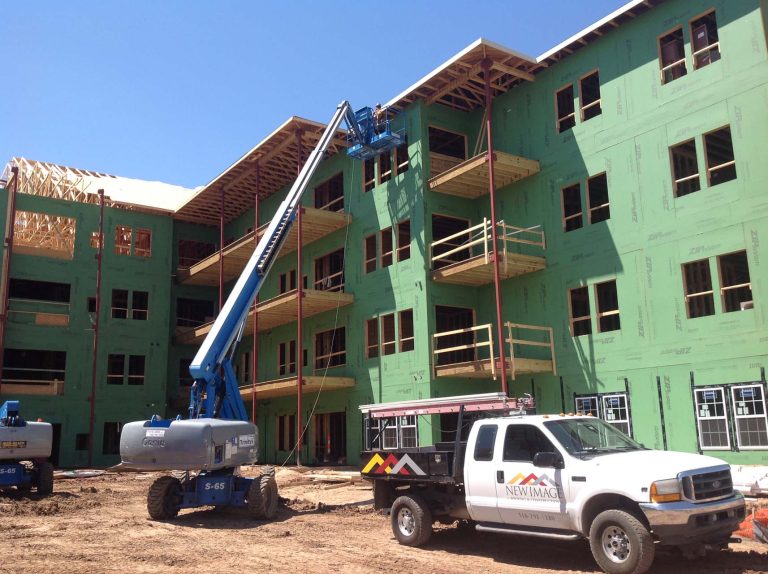 a crane lifts a worker to the top of a building for roof installation