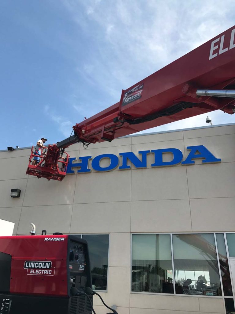 A crane lifts a worker up to the top of a Honda dealership roof