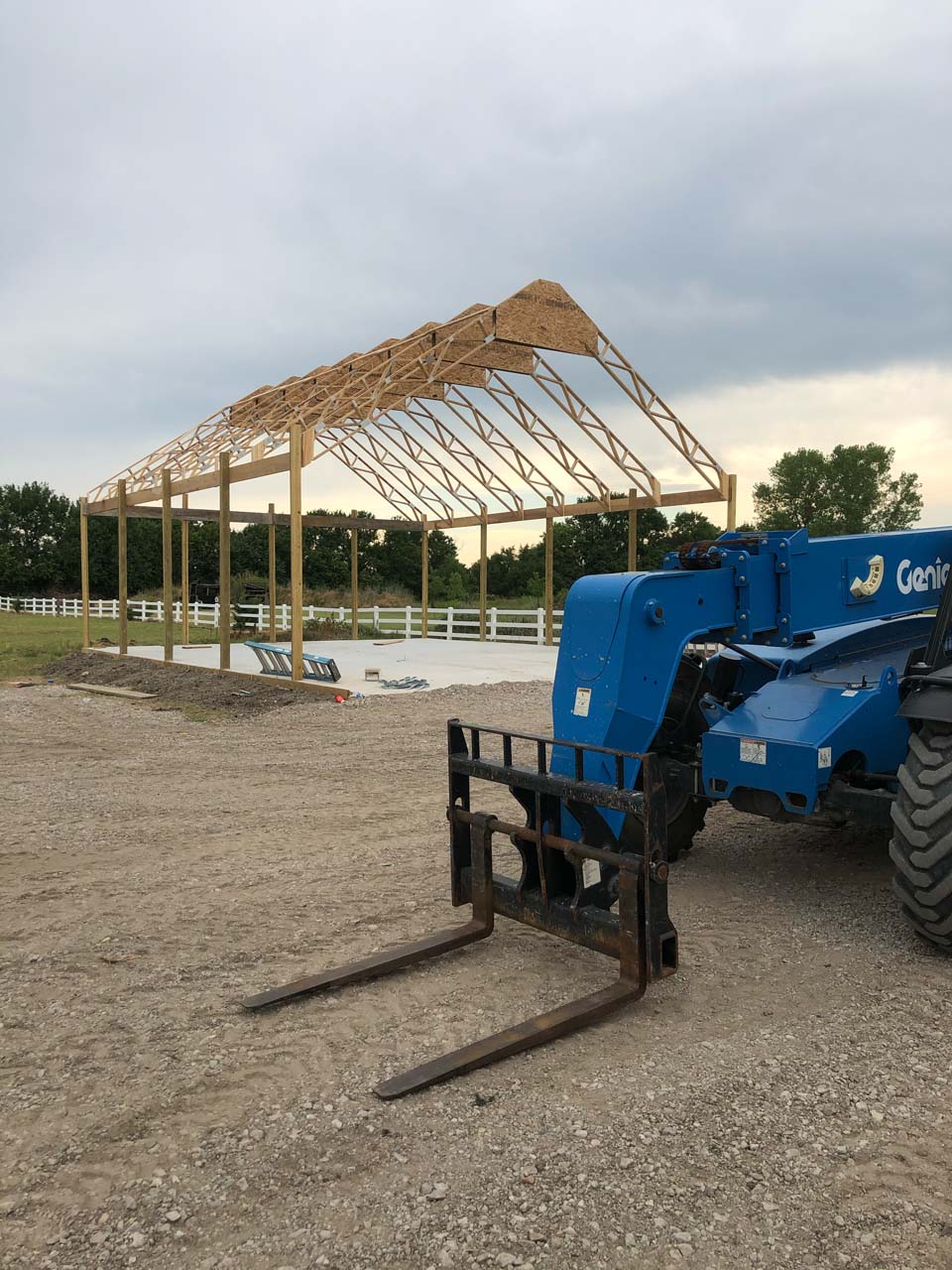 The frame of a metal building stands in a field with a pallet mover
