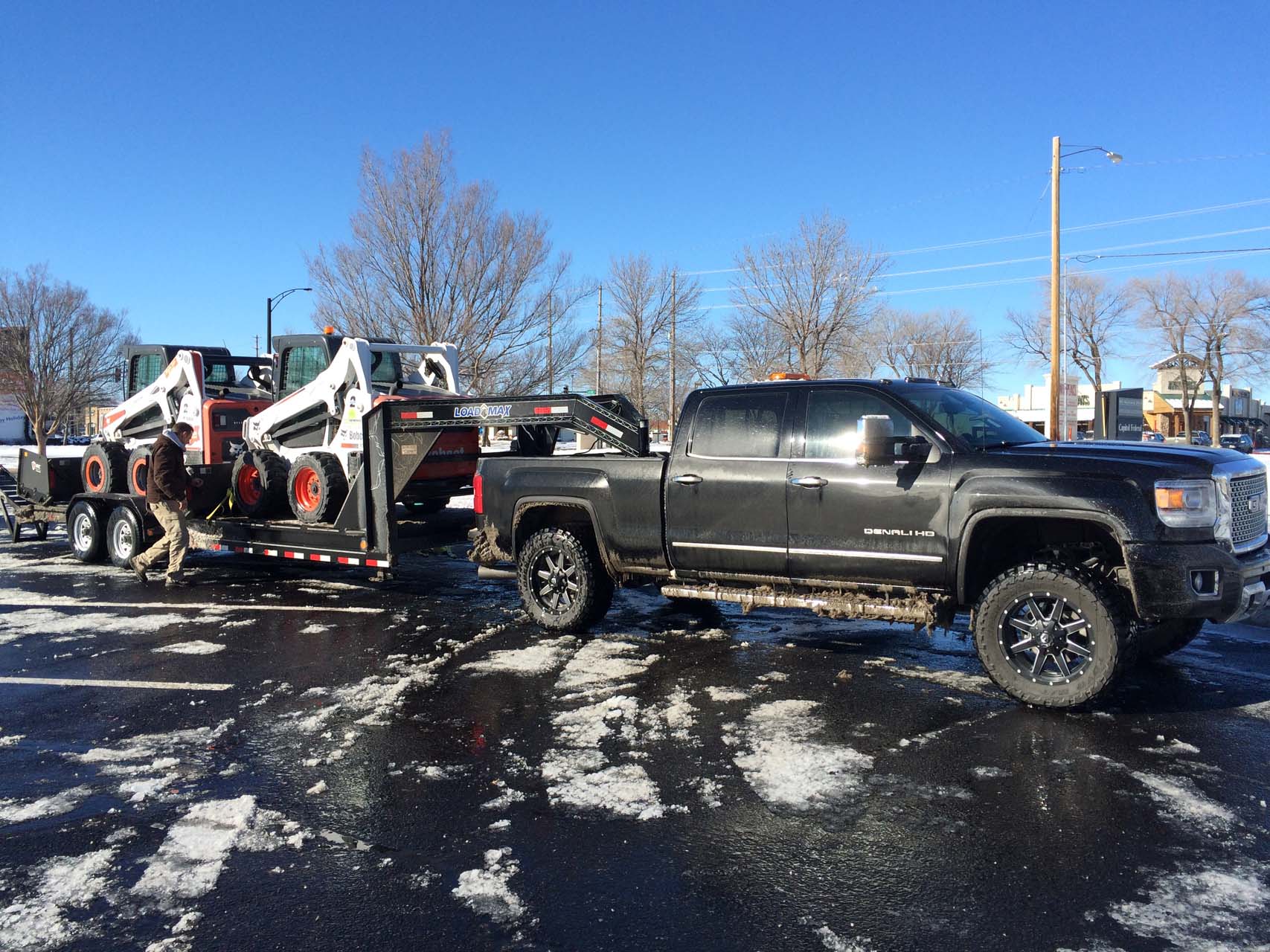 a black truck pulls a trailer of snow removal vehicles